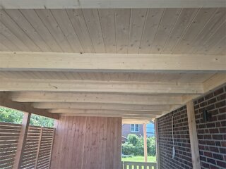 Innenansicht eines Carports mit Flachdach, heller Holzdecke und geschlossener Rückwand