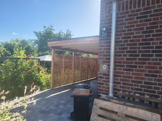 An ein Backsteinhaus angebauter Carport mit Flachdach und Holzlamellen