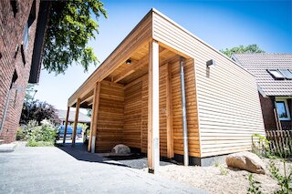 Moderner Holzcarport mit senkrechten Stützen, Holzfassade und integriertem Geräteraum