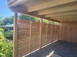 Seitenansicht eines Carports mit waagerechten Holzlamellen und sichtbarer Holzbalkendecke