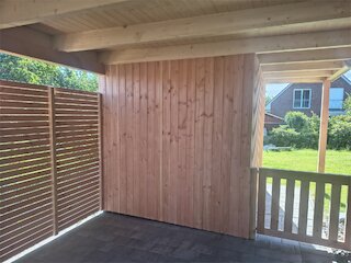 Innenansicht eines Carports mit Holzverkleidung, Lamellenwand und Durchgang zum Garten