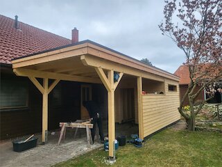 An ein Wohnhaus angebauter Holzcarport mit Satteldach und roten Dachziegeln