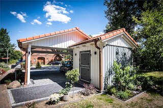 Seitlich angebauter Carport mit Satteldach neben einem Haus mit weißer Holzfassade