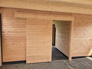 Holzverkleideter Geräteraum mit Türöffnung als Teil eines Doppelcarports
