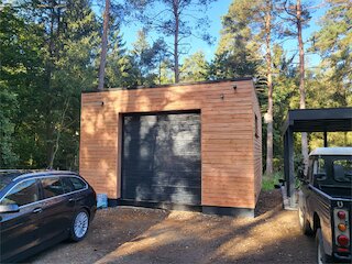 Freistehende Holzgarage mit Flachdach und dunklem Garagentor auf einem Waldgrundstück