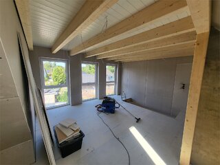 Innenausbau unter einem sanierten Dach mit sichtbaren Holzbalken und neuen Trockenbauwänden