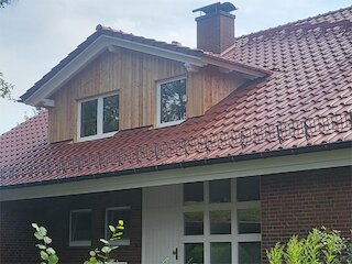 Dachgaube mit senkrechter Holzfassade und Fenstern auf einem roten Ziegeldach