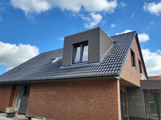 Moderne Flachdachgaube mit dunkler Holzfassade und großen Fenstern auf einem Wohnhaus