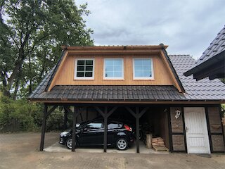 Breite Schleppdachgaube mit Holzfassade und drei Fenstern über einem Carport