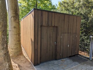 Geräteschuppen aus senkrechten Holzbohlen mit Doppeltür zwischen Bäumen