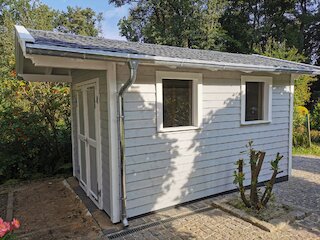 Grau gestrichenes Gartenhaus aus Holz mit Pultdach, Dachrinne und zwei Fenstern