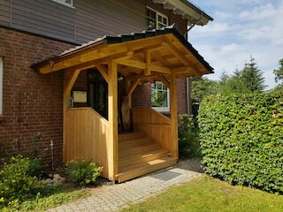 Hauseingang mit Vordach aus Holz, seitlichem Windschutz und kleiner Treppe