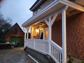Weiß gestrichenes Holzvordach an einem Backsteinhaus mit Geländer und Beleuchtung