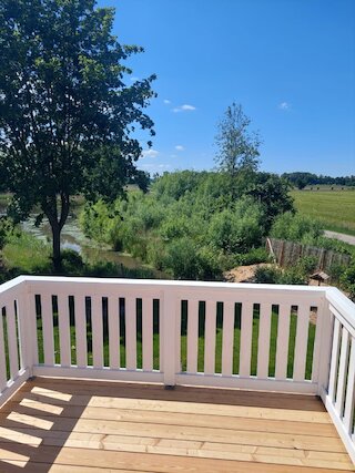 Blick von einem Holzbalkon mit weißem Geländer in einen grünen Garten