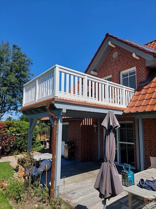 Weißer Holzbalkon mit Stützkonstruktion und Sitzplatz an einem Backsteinhaus