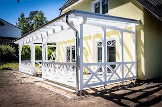 Weiße Terrassenüberdachung aus Holz mit Geländer an einem Wohnhaus