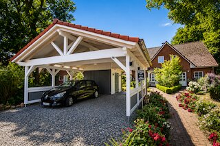 Weißer Holzcarport mit Satteldach und integriertem Abstellraum vor einem roten Backsteinhaus