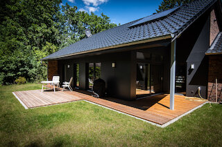 Überdachte Holzterrasse an einem dunkel verkleideten Wohnhaus