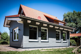 Eingeschossiger Holzanbau mit grauer Holzfassade und rotem Ziegeldach