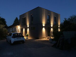 Beleuchteter Holzanbau mit dunkler Holzfassade am Abend