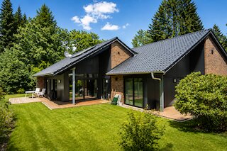 Modernes Wohnhaus mit dunkler Fassade, Satteldächern und umlaufender Holzterrasse im Garten