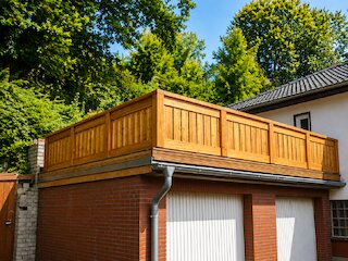 Holzterrasse auf einer Garage mit umlaufendem Holzgeländer vor dichtem Baumbestand